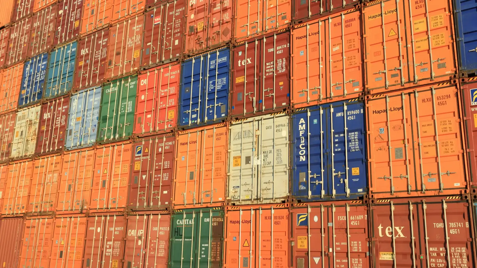 A wall of stacked shipping containers in red, blue, green and orange.
