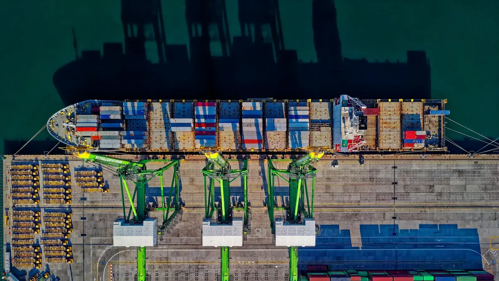 Seen from above, a container ship alongside the quay with cranes loading it.
