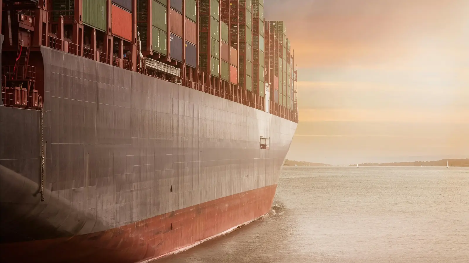 The hull of a loaded container ship at sea in early morning light.